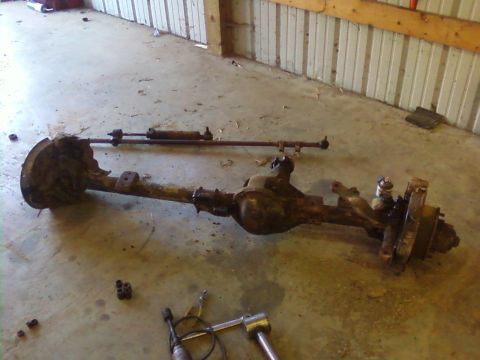 1995 Ford Bronco - A disassembled front axle assembly rests on a concrete floor inside a garage or workshop.