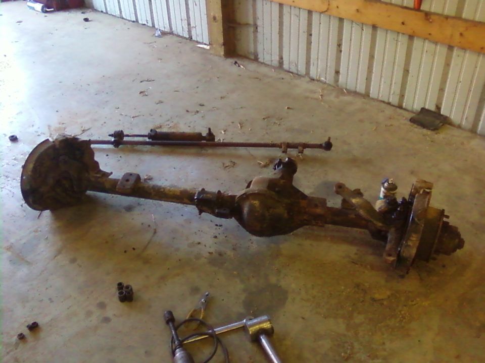 Front axle assembly with steering linkage removed, sitting on a concrete floor
