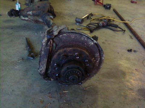 1995 Ford Bronco - A heavily rusted front axle assembly, likely from an older vehicle, lies on a workshop floor.