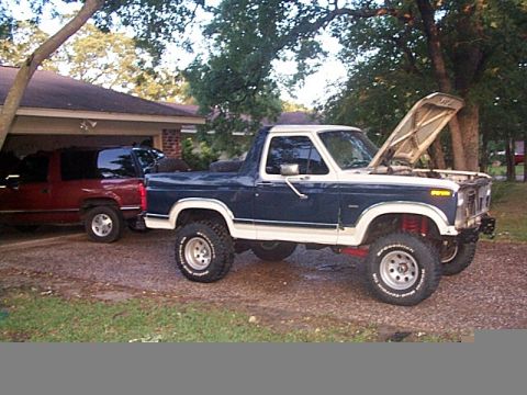 1986 Ford Bronco - This lifted 1986 Ford Bronco is parked next to another vehicle under a carport.