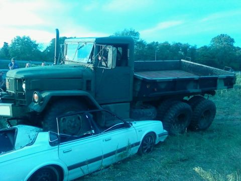 1990 Ford Bronco - A military dump truck is parked next to a white sedan in an outdoor setting.