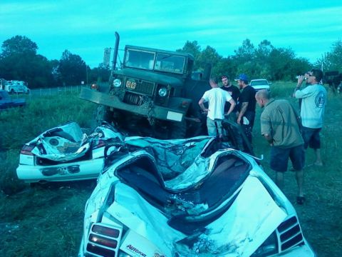 1990 Ford Bronco - A military truck appears to have driven over two severely damaged cars in a grassy field.