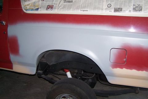 1990 Ford Bronco - Vehicle body is being prepped for paint, with primer applied to the rear quarter panel and red paint visible on the upper section.