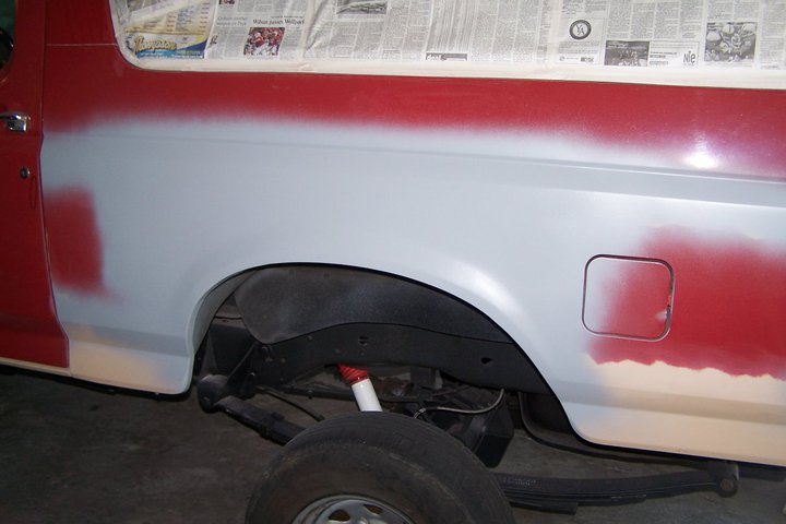 Side view of vehicle body with primer and red paint, undergoing prep work