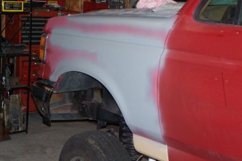 1990 Ford Bronco - Side view of a 1990 Ford Bronco's fender and door, showing primer and red paint.