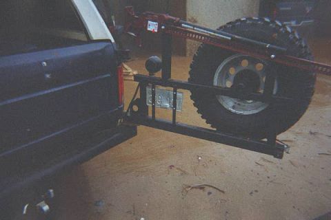 1986 Ford Bronco - The rear of a dark SUV is shown with a spare tire mounted on a carrier, along with a jack and a license plate.