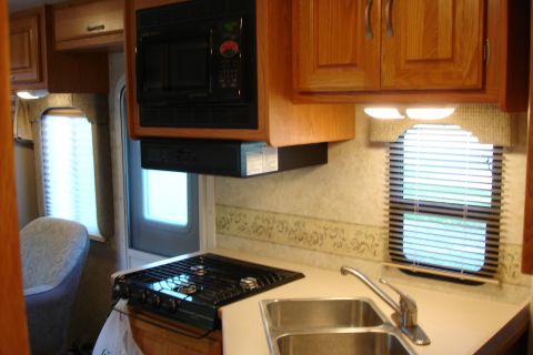 2005 Chevrolet Silverado 3500 - Interior view of an RV kitchen a microwave, a three-burner stovetop, and a stainless steel sink.