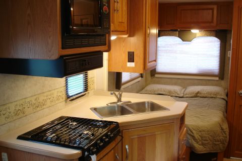 2005 Chevrolet Silverado 3500 - Interior view of an RV, a kitchen area with a sink and stove, and a bed in the background.