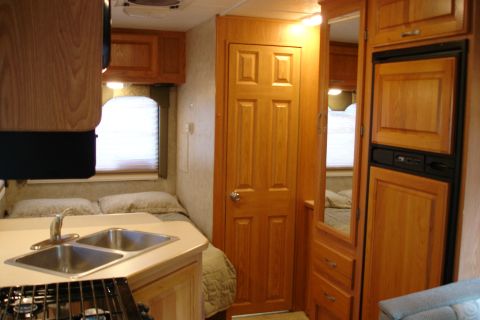 2005 Chevrolet Silverado 3500 - The interior of an RV features a bed, kitchen area with a sink, and wooden cabinetry.