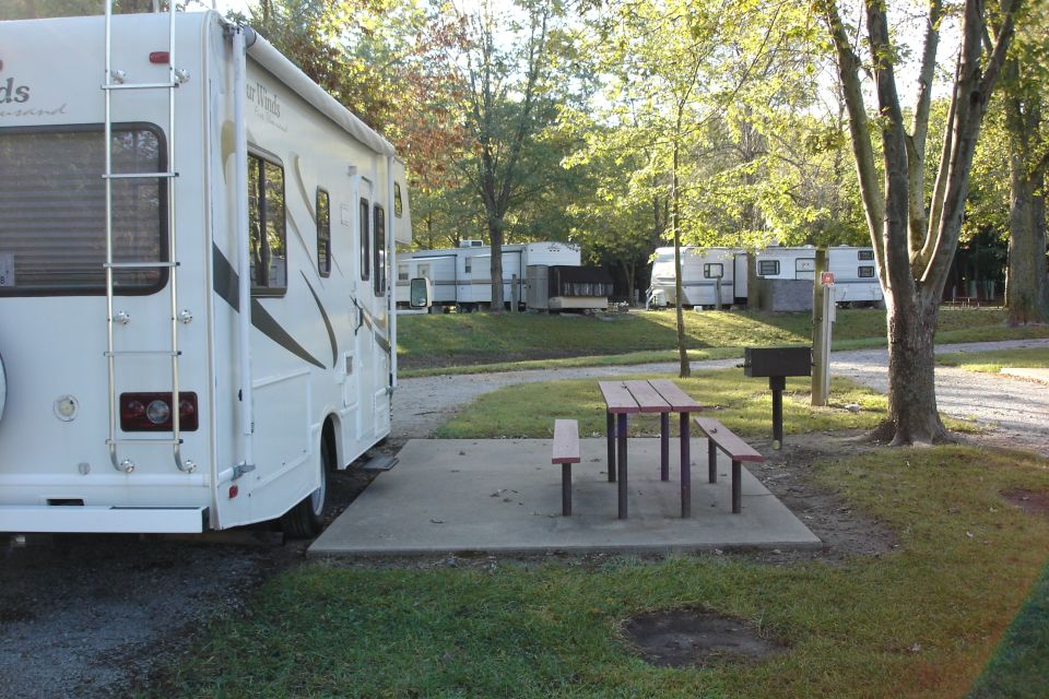 RV parked at a campsite with a picnic table and grill. Other RVs are visible in the background