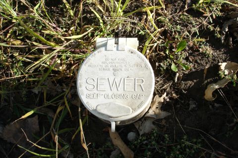 2005 Chevrolet Silverado 3500 - A white sewer cap is visible on the ground, surrounded by grass and dirt.