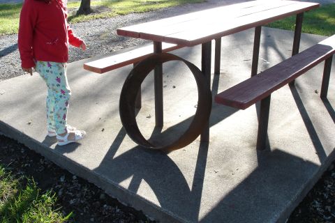 2005 Chevrolet Silverado 3500 - A picnic table sits on a concrete pad with a large metal ring as decoration. A child stands nearby.