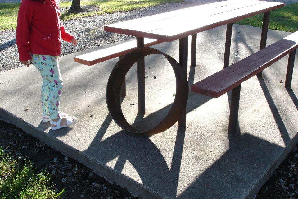 Child standing by a picnic table with a large metal ring on the concrete pad