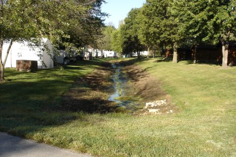 2005 Chevrolet Silverado 3500 - A campground scene with multiple RVs and cabins visible, bordered by trees and a dry creek bed.