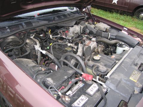 1991 Ford LTD Crown Victoria - The engine compartment of a maroon sedan is shown, with another vehicle partially visible behind it.
