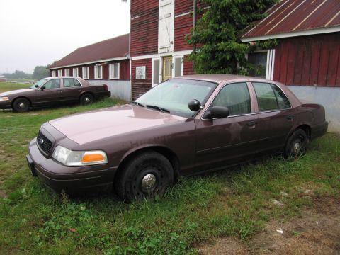 1991 Ford LTD Crown Victoria - Two brown Ford Crown Victorias are parked on the grass in front of a red barn.