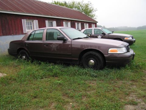 1991 Ford LTD Crown Victoria - Two Ford Crown Victoria police cars are parked in front of a red barn on a foggy day.