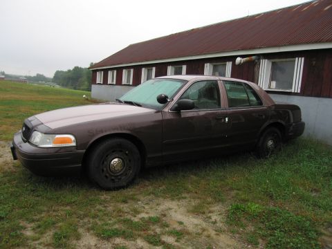 1991 Ford LTD Crown Victoria - A brown Ford Crown Victoria is parked next to a red building with white-trimmed windows.