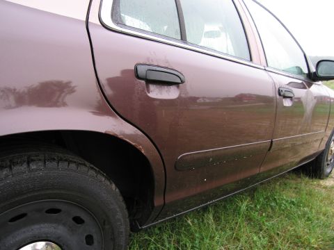1991 Ford LTD Crown Victoria - The rear side of a brown sedan shows rust and damage to the body panels.