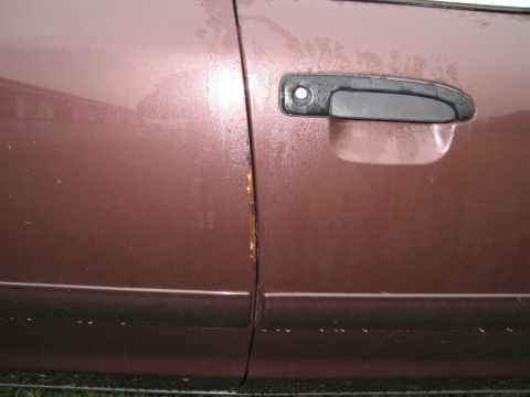 1991 Ford LTD Crown Victoria - Close-up of a brown car door, showing a black handle and visible rust along the panel seam.