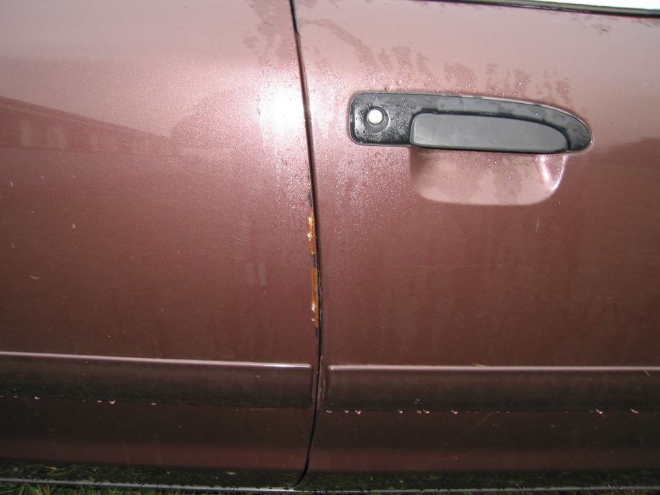 Brown car door with rust near the seam and a black door handle