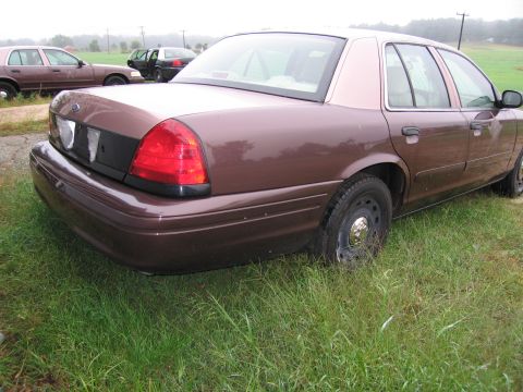 1991 Ford LTD Crown Victoria - Rear view of a brown Ford Crown Victoria with another Crown Victoria and a dark SUV visible in the background.