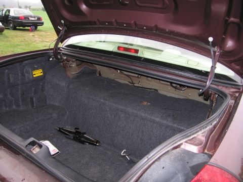 1991 Ford LTD Crown Victoria - The trunk of a maroon sedan is open, revealing the spare tire and jack. Another car is visible in the background.
