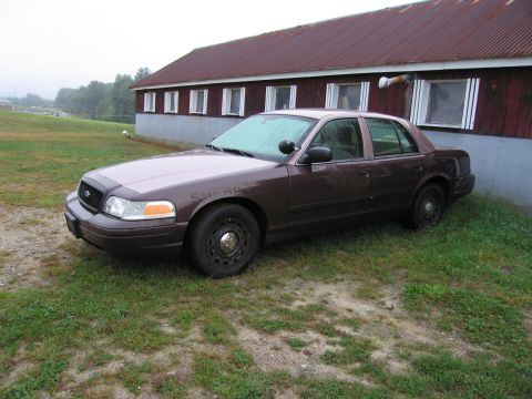 1991 Ford LTD Crown Victoria - A brown Ford Crown Victoria sedan, marked as "SHERIFF", is parked on a grassy area next to a red barn.