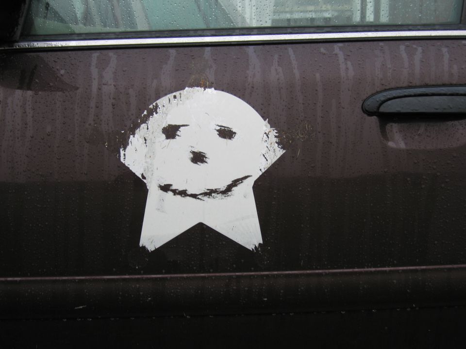 White sticker of a cartoon face on a dark car door, with water droplets on the surface