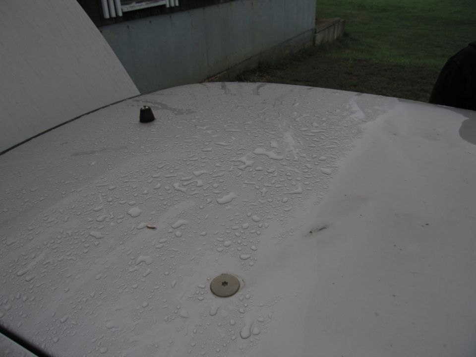 Car roof covered in water droplets, with an antenna and a circular fixture visible