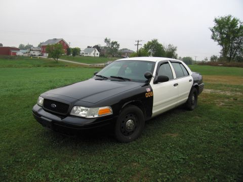 1991 Ford LTD Crown Victoria - This police car has a two-tone paint scheme and is parked in a grassy area with buildings in the distance.