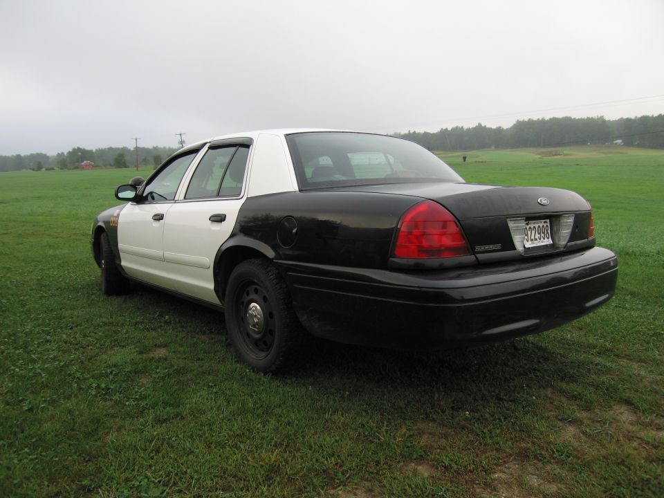 Two-tone police car with black rear and white front, parked on grass