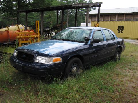 1991 Ford LTD Crown Victoria - A Ford Crown Victoria sedan sits parked outdoors in a grassy area with various equipment nearby.