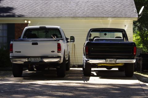 1999 Ford F-250 - Two pickup trucks, a white Ford F-250 and a black truck, are parked in front of a house.