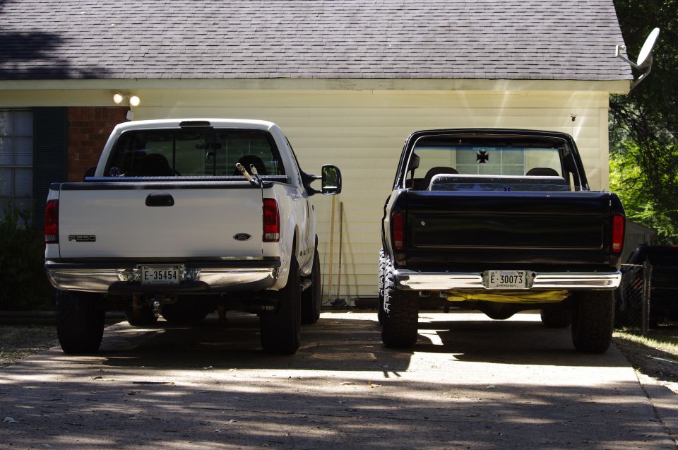 White 1999 Ford F-250 pickup truck parked next to a black pickup truck, rear view