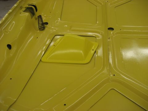 1978 Ford Bronco - The underside of a yellow car hood shows structural reinforcements and a vent cover.