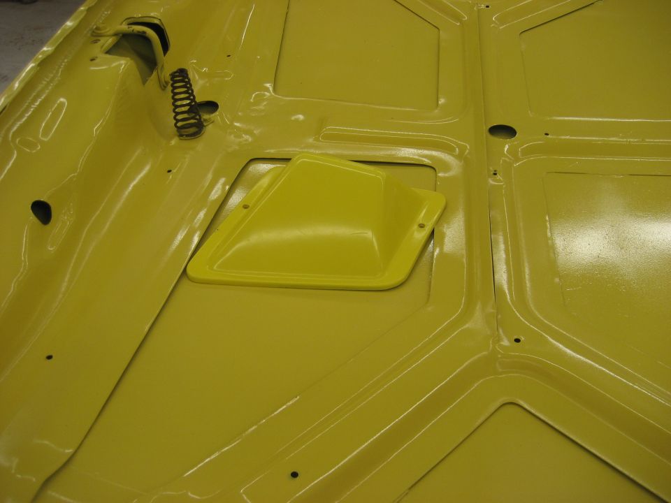underside of a yellow car hood with a spring and a raised vent cover