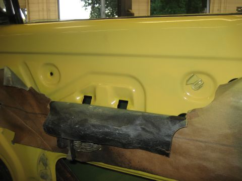 1978 Ford Bronco - Interior view of a yellow door panel, showing exposed insulation and black trim pieces.