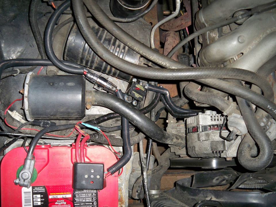 Engine bay with red battery, alternator, and various hoses and wiring