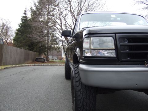 1995 Ford F-150 - The front end of a black Ford F-150 is visible from a low angle, parked on a residential street.