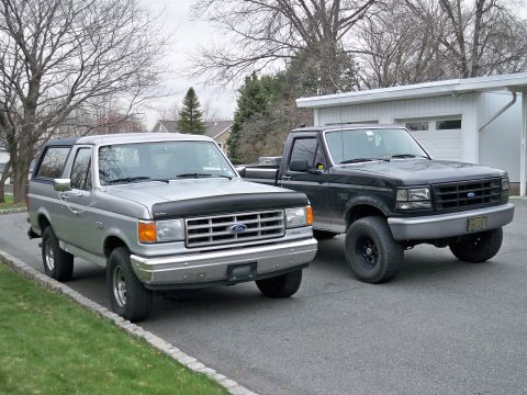 1995 Ford F-150 - A silver 1995 Ford Bronco and a black 1995 Ford F-150 pickup are parked in front of a garage.