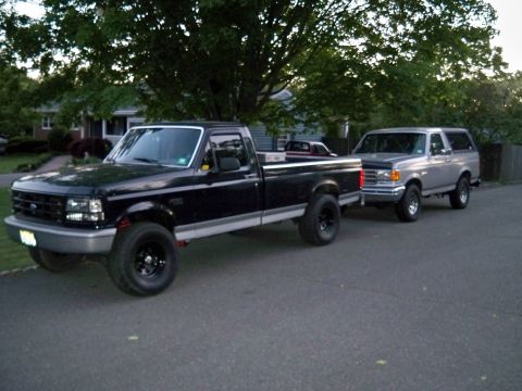 1995 Ford F-150 - A black Ford F-150 pickup truck is parked on a street, towing a silver Ford Bronco behind it.