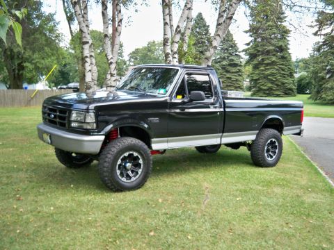 1995 Ford F-150 - This lifted 1995 Ford F-150 pickup truck is parked on a grassy lawn with trees in the background.