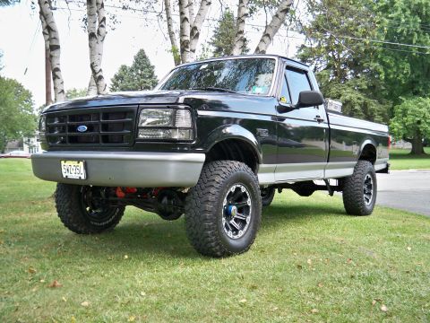 1995 Ford F-150 - This lifted Ford F-150 pickup truck is shown from a three-quarter front view, parked on a grassy area.