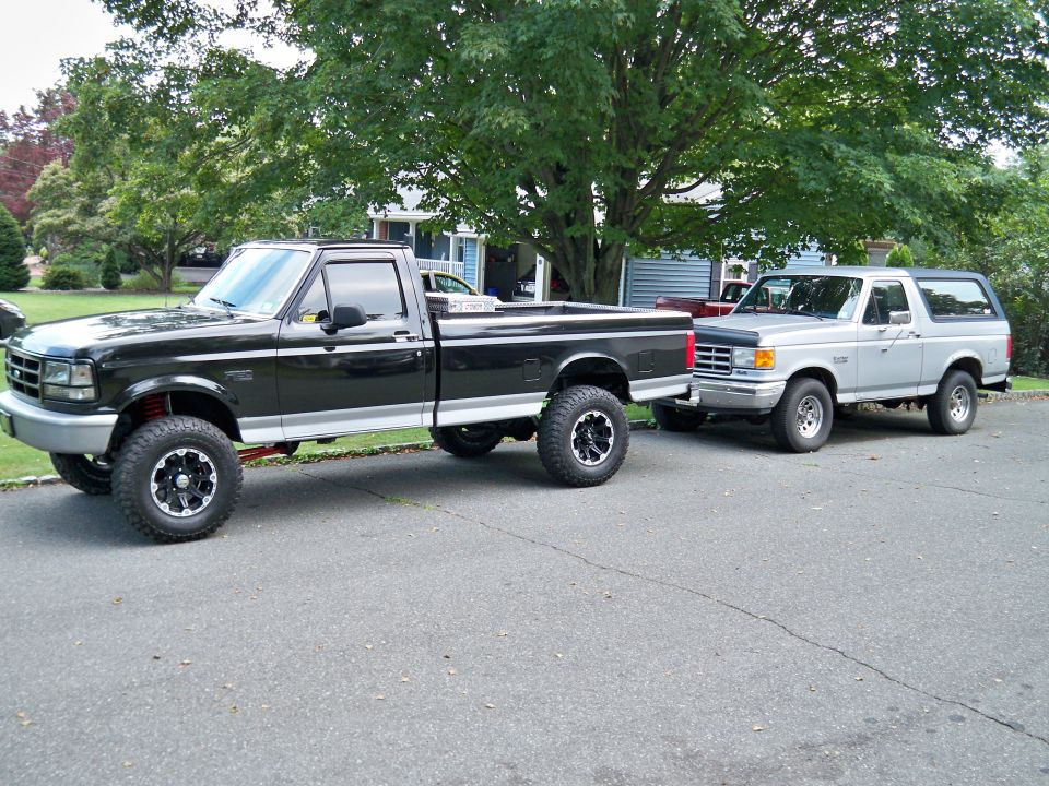 Black Ford F-150 pickup truck and silver Ford Bronco parked on a residential street