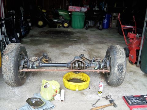 1995 Ford F-150 - A disassembled front axle assembly sits on a garage floor, surrounded by tools and automotive fluids.