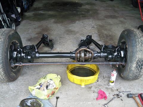 1995 Ford F-150 - A vehicle's rear axle assembly is shown with the differential cover removed, sitting on a concrete surface with tools and an oil pan nearby.