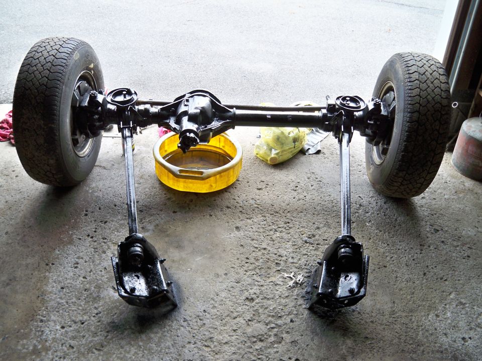 Rear axle assembly with two wheels, a yellow oil drain pan, and a yellow plastic bag on concrete