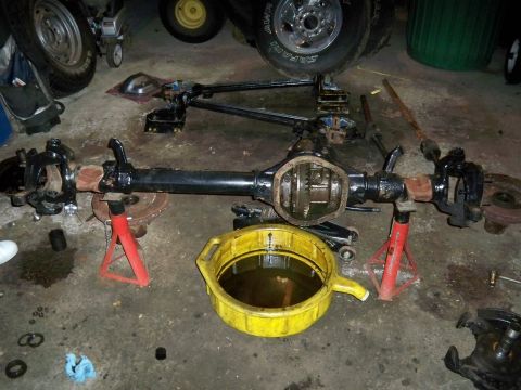 1995 Ford F-150 - Vehicle axle assembly disassembled and supported on jack stands, with a drain pan catching fluid.