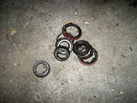 1995 Ford F-150 - Several worn wheel bearings and seals are piled on a concrete surface, likely removed during a vehicle repair.